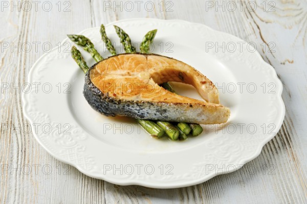 A gourmet dish features a beautifully grilled salmon steak served alongside fresh green asparagus