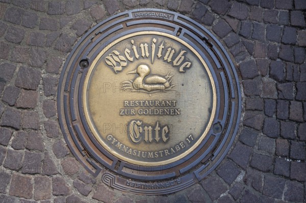 Municipal manhole cover with an advert for a wine bar, Biberach an der Riß, Baden-Württemberg, Germany