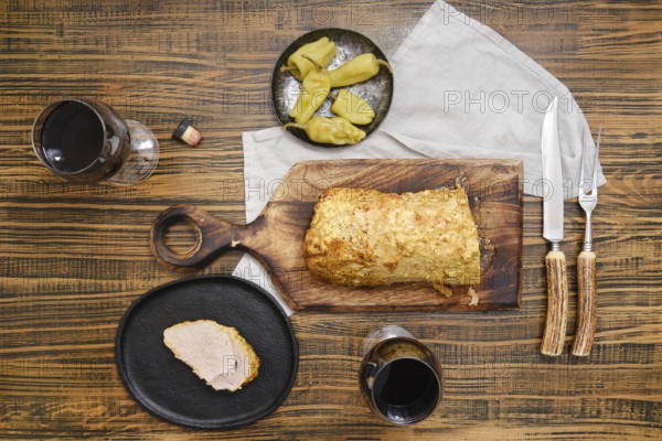 Overhead view of roasted pork meat and pickled peppers on a wooden table accompanied with red wine in glasses