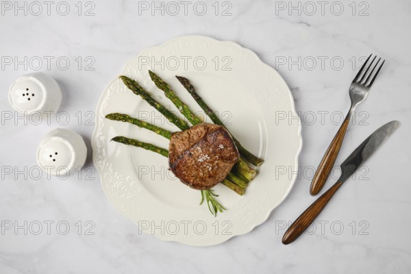 Savor a perfectly cooked filet mignon paired with tender asparagus stalks on a decorative white plate. The meal is elegantly presented with salt and pepper shakers in the background