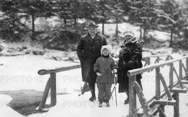 Winter excursion, 1930s, Three people in winter clothing stand on a snow-covered bridge in front of a wooded background, Historical photo