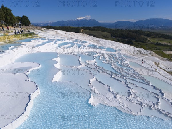 Wide view over white cascade terraces with turquoise blue water against a mountain backdrop, aerial view, sinter terraces, lime sinter terraces, travertine terraces, Pamukkale, Denizli, UNESCO World Heritage Site, Anatolia, Turkey