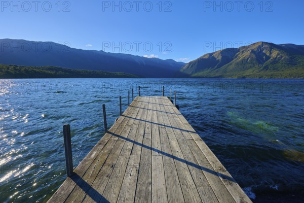 A narrow footbridge leads into the blue waters of a lake, surrounded by an impressive mountain landscape, summer, Lake Rotoiti, Saint Arnaud, Tasman Region, South Island, New Zealand