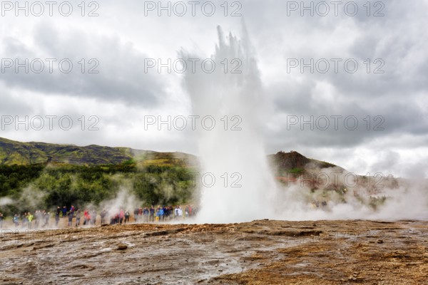 Active Strokkur, tourists observe eruption, high temperature area Haukadalur, tourist attraction at the Golden Circle, Sudurland, Iceland