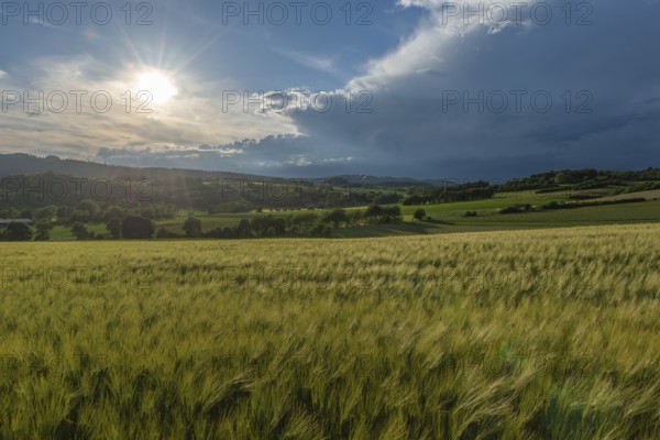 Dramatic cloudy sky with approaching storm and last sunbeams, Frankenhain, dark cloud wall, cumulonimbus and cumulus clouds, sunbeams, thunderstorm in the lift, low mountain landscape, agriculture, forest, grain field, backlight shot, municipality of Berkatal, Werra-Meissner-Kreis, Hesse, Germany
