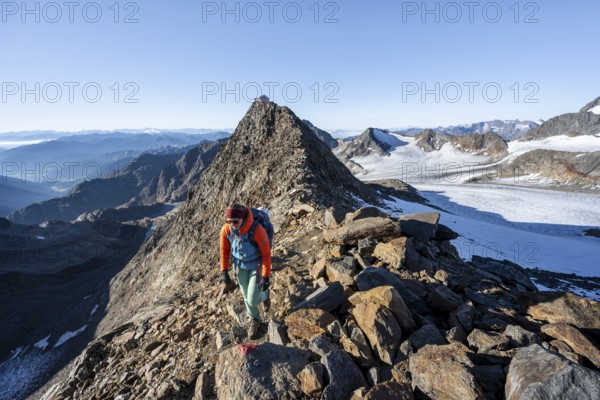 Mountaineer on a rocky ridge, ascent to the Wilder Freiger, summit of the Becher with Becherhaus behind, picturesque high mountain landscape, view of the Übeltalferner glacier and rocky mountain peaks, Stubai Alps, South Tyrol, Italy