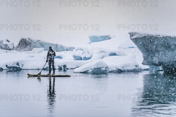 Man stand up paddling, snowfall, glacier lagoon Jökulsarlon at Vatnajökull, Iceland* Man stand up paddling on glacier lagoon Jokulsarlon at Vatnajokul, snowfall, Iceland