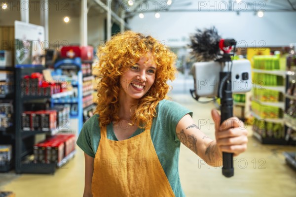 Young woman working as supermarket clerk vlogging using smartphone and microphone promoting products on social media