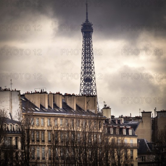 With a dramatic overcast sky, the Eiffel Tower rises impressively above the historic buildings of Paris, showcasing the city's unique blend of architecture and atmosphere. France