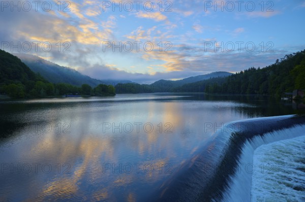 Calm lake with dam Paulushof-Absperrdamm, at dusk, surrounded by mountains and forests under a cloudy sky, summer, Rursee, Obersee, Rurberg, Simmerath, Eifel National Park, North Rhine-Westphalia, Germany