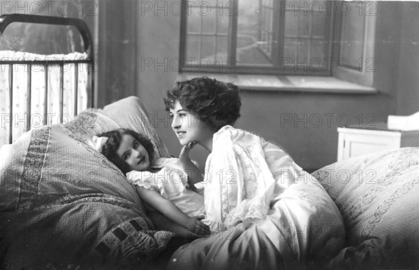 Woman with daughter, 1920s, A mother lies down with her child in bed, showing affection in a cosily furnished room, Historical photo
