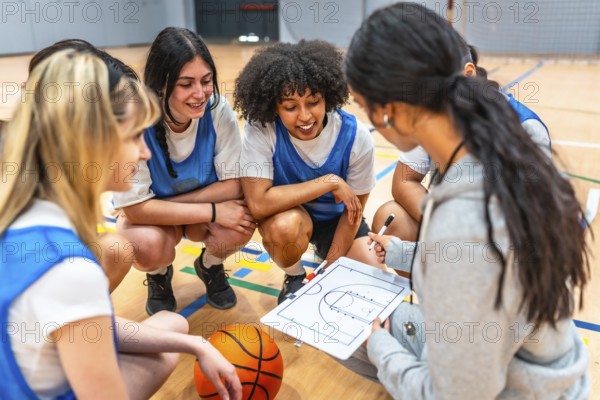 Basketball coach explaining game strategy to her young female athletes on a clipboard in a gym