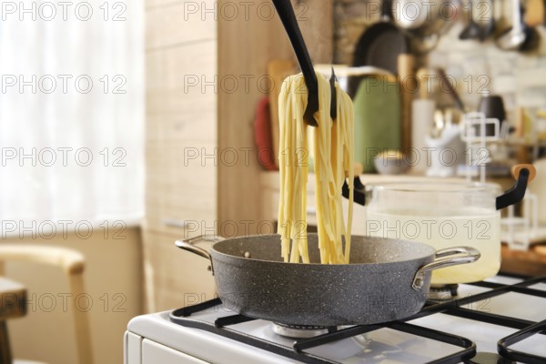 A person lifts cooked spaghetti from a pot using a utensil, with steam rising in a cozy kitchen. Natural light filters through a window, illuminating the surroundings and creating a warm atmosphere