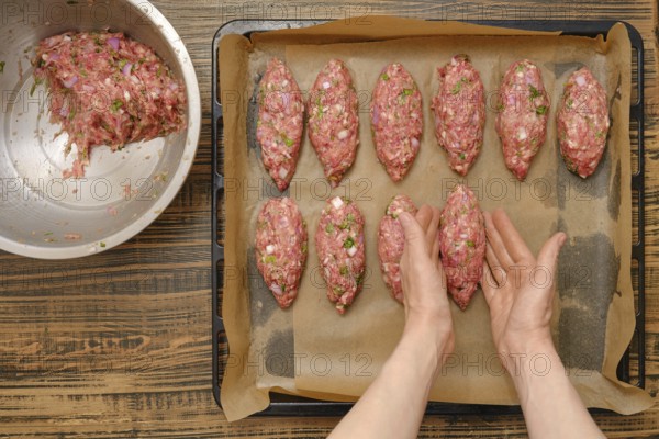 Freshly shaped kebabs are arranged on a baking tray lined with parchment paper. A mixing bowl filled with seasoned meat sits nearby in a warm kitchen, indicating a cooking process in progress