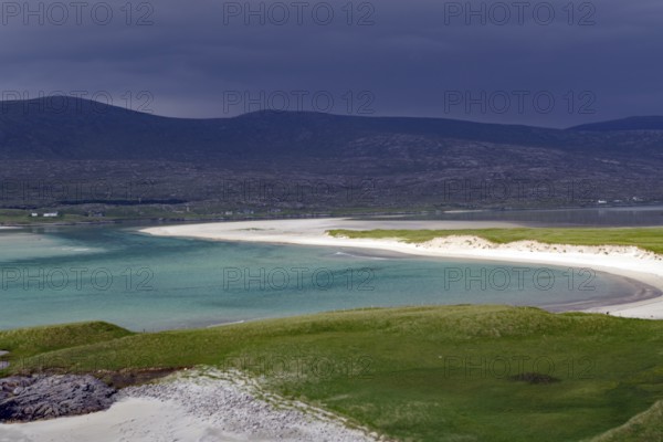 A tranquil beach with turquoise waters and dark, cloudy skies at the foot of mountains, Isle of Harris, Hebrides, Scotland, United Kingdom