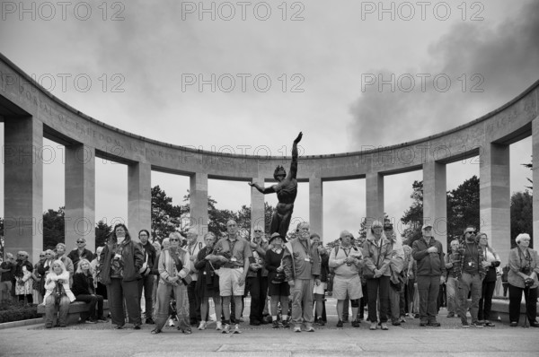 Funeral service, mourning relatives pause during the playing of the US national anthem, bronze statue The Spirit of American Youth Rising from the Waves by Donald De Lue, military cemetery, Normandy American Cemetery and Memorial, Omaha Beach, D-Day, Operation Overlord, Saint-Laurent-sur-Mer near Colleville-sur-Mer, black and white, Normandy, Calvados, France