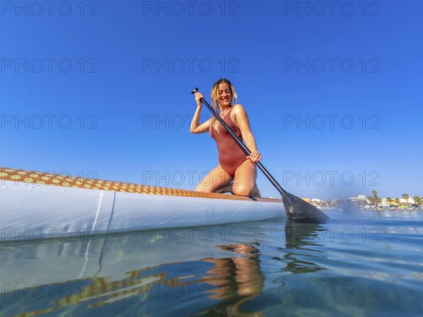 Young woman paddling on a stand up paddle board on a sunny summer day, enjoying the calm blue water