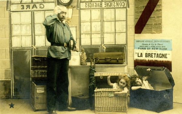 2 children in boxes, 1920, A man poses in a railway station environment while children humorously peer out from inside suitcases, historical photo