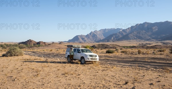 Tourist with off-road car on a sandy track, rock formation, Brandberg, Damaraland, Namibia
