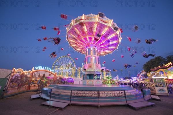 Brightly illuminated carousel turns at a night fair, chain carousel, spring festival, Cannstatter Wellenflug, blue hour, Cannstatter Wasen, Bad Cannstatt, Stuttgart, Baden-Württemberg, Germany