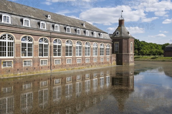 Historic brick building reflected in calm water under a blue sky and clouds, Nordkirchen Castle, Nordkirchen, Münsterland, North Rhine-Westphalia, Germany