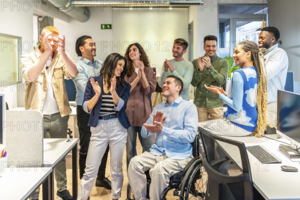 Group of happy multi ethnic colleagues clapping, celebrating a great achievement together with their coworker in a wheelchair in their bright modern office