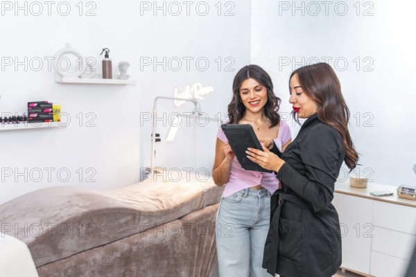Beautician and customer discussing treatment options while using a digital tablet in a modern, elegant beauty salon environment