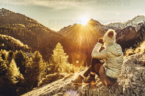 Woman sitting thoughtfully at a feslen at autumn atmosphere during sunset in the Swiss Alps in the Engadine. Photographed from the village of Maloja on the Maloja Pass