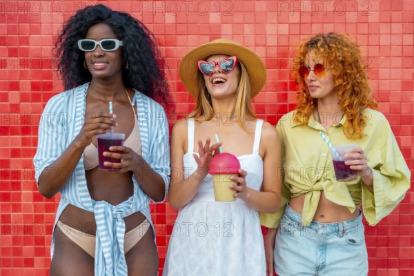 Three diverse women enjoying refreshing drinks against a vibrant red wall, celebrating summer and friendship
