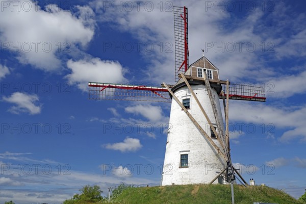 White painted windmill with red wings in front of a blue sky, Bruges, Belgium