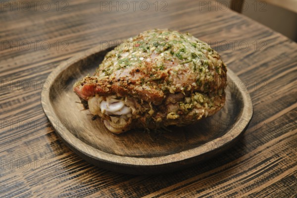 A roasted turkey thigh on a round wooden plate. The thigh is seasoned with fresh herbs, showcasing its crispy skin and juicy meat, perfect for a festive dinner or gathering