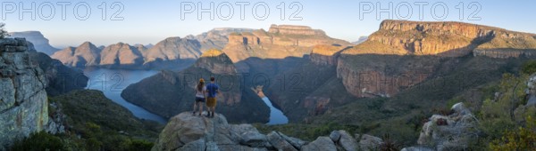 Two hikers enjoying the panorama, sunset at Blyde River Canyon with Three Rondawels peak, view of canyon with Blyde River and table mountains in the evening light, canyon landscape, Panorama Route, Mpumalanga, South Africa