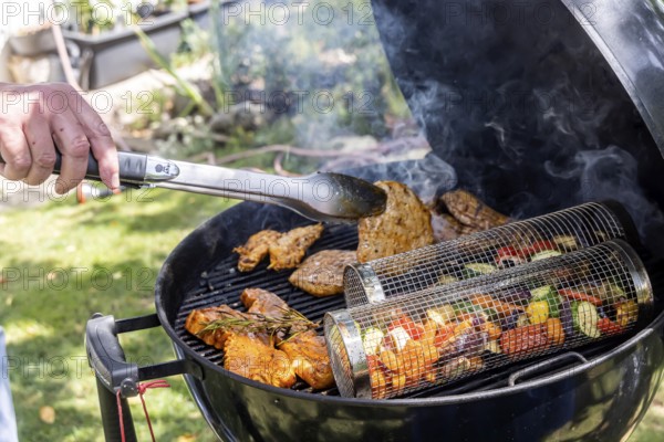 Barbecue in the garden. Meat and vegetables, vegetarian and vegan, are served on the kettle grill. Barbecue baskets for gently braising carrots, courgettes or peppers are right on trend. Münsingen, Baden-Württemberg, Germany