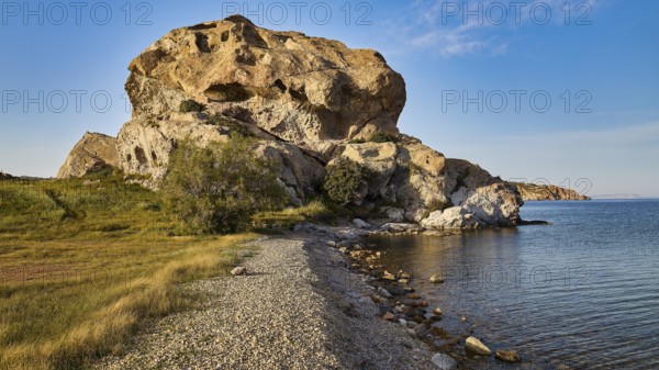 Large rock formation on the coast with clear sky and grassy areas in the foreground, Rock of Kalikatsou, Patmos, Dodecanese, Greek Islands, Greece