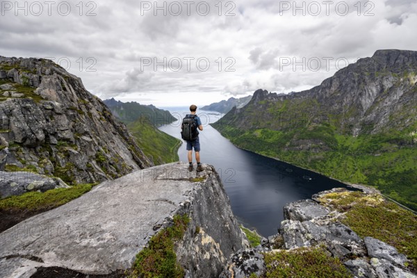 View of Øyfjorden fjord and mountains, view from Barden mountain, young man standing on a cliff, Senja, Norway