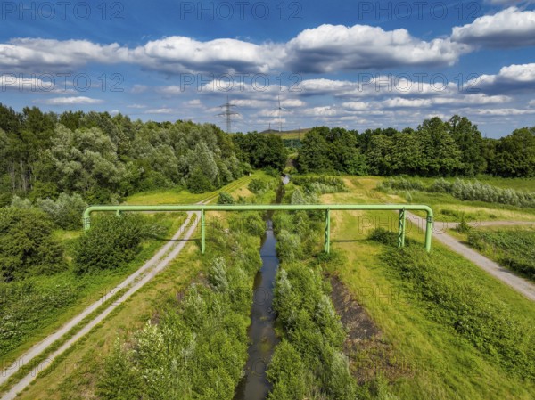 Bottrop, North Rhine-Westphalia, Germany - Renaturalised Boye, the tributary of the Emscher, has been transformed into a near-natural watercourse, flood protection through newly designed flooding areas, the Boye is now free of wastewater following the construction of a parallel sewer, is part of the Emscher river system and thus part of the Emscher conversion, was previously an open, above-ground wastewater channel, mixed water channel with surface water and wastewater. Wind turbine on the Mottbruch spoil tip at the back