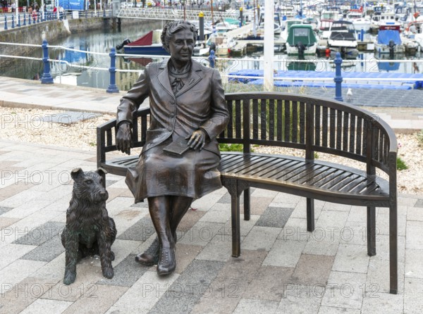 Bronze sculpture statue artwork Agatha Christie sitting on bench with her dog, Torquay, Devon, England, UK by artist Elisabeth Hadley 2024