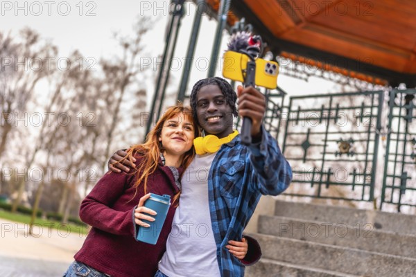 Two young content creators are recording a video blog in a park, using a smartphone attached to a gimbal with external microphone