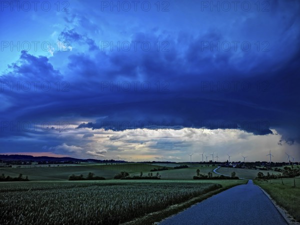 Aufziehendes Gewitter mit imposanter und bedrohlicher Wolkenformation einer Gewitterzelle über einem Dorf mit Windrädern im Hintergrund, Baden-Württemberg, Deutschland