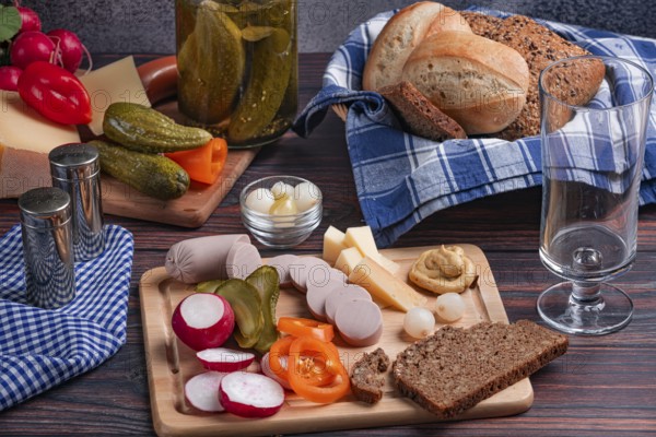 Rustic snack with sausage, cheese, vegetables, mustard and bread on a laid table