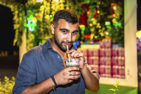 Young man sips a mojito through a straw at a vibrant night market, enjoying the festive atmosphere