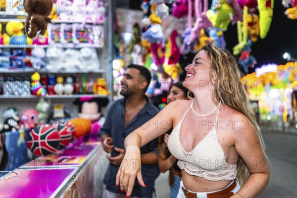 Happy friends playing at a throwing game stall trying to win plush toys at amusement park at night
