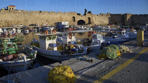 Boats moored in the harbour in front of an old wall under a blue sky, Rhodes Old Town, Rhodes, Dodecanese, Greek Islands, Greece