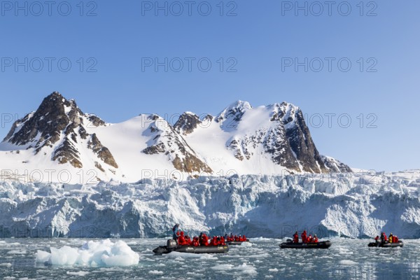 Group of Zodiacs in front of glacier and mountain range with snow, sea, Fugelfjorden, Spitsbergen, Svalbard