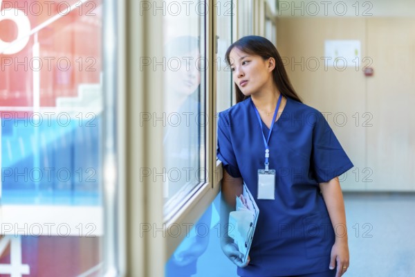 Thoughtful medical professional pausing in hospital hallway, holding patient files and gazing outside with a contemplative expression