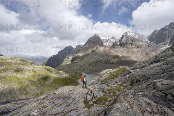 Mountaineer on a rocky hiking trail, view of the turquoise-blue mountain lake Großer Gradensee, behind her the summit of the Petzeck, Hoher Perschitzkopf and Kruckelkopf, Schober Group, Hohe Tauern National Park, Carinthia, Austria