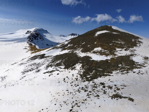 Near a snow-covered hilltop with rocks on the descent under a clear sky, aerial view, Aragaz, Aragac, Alagyaz, extinct stratovolcano, 4090 m, Aragazotn, Shirak, Armenia