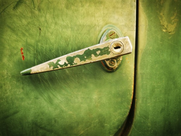 A close-up view highlights a vintage green metal latch on a door, showcasing its worn texture and the rustic charm of peeling paint against the muted background