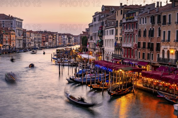 View of the Grand Canal with gondoliers at sunset, picturesque evening mood with illuminated palazzos on the canal, long exposure, view from the Rialto Bridge, Venice, Veneto, Italy