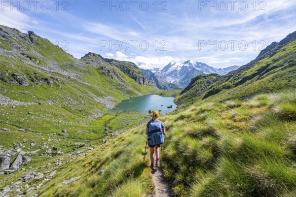 Mountaineer on hiking trail in picturesque mountain landscape, view of mountain lake Lac du Louvie and glaciated mountain peaks of the Grand Combine, Valais Alps, Val de Bagnes, Valais, Switzerland